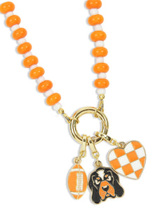 An orange and white beaded necklace with gold-tone hardware, featuring three dangling charms: a football, a black-and-orange dog portrait, and an orange-and-white checkered heart.
