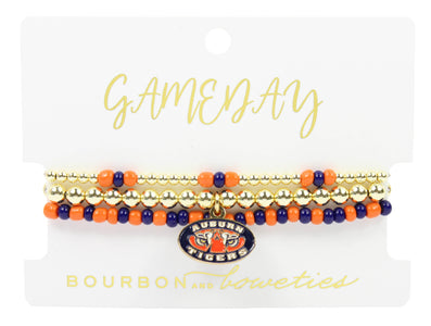 A set of three beaded stretch bracelets displayed on a white branded card. The bracelets feature gold-tone beads, orange and navy blue beads, and a central oval charm with the Auburn Tigers logo.